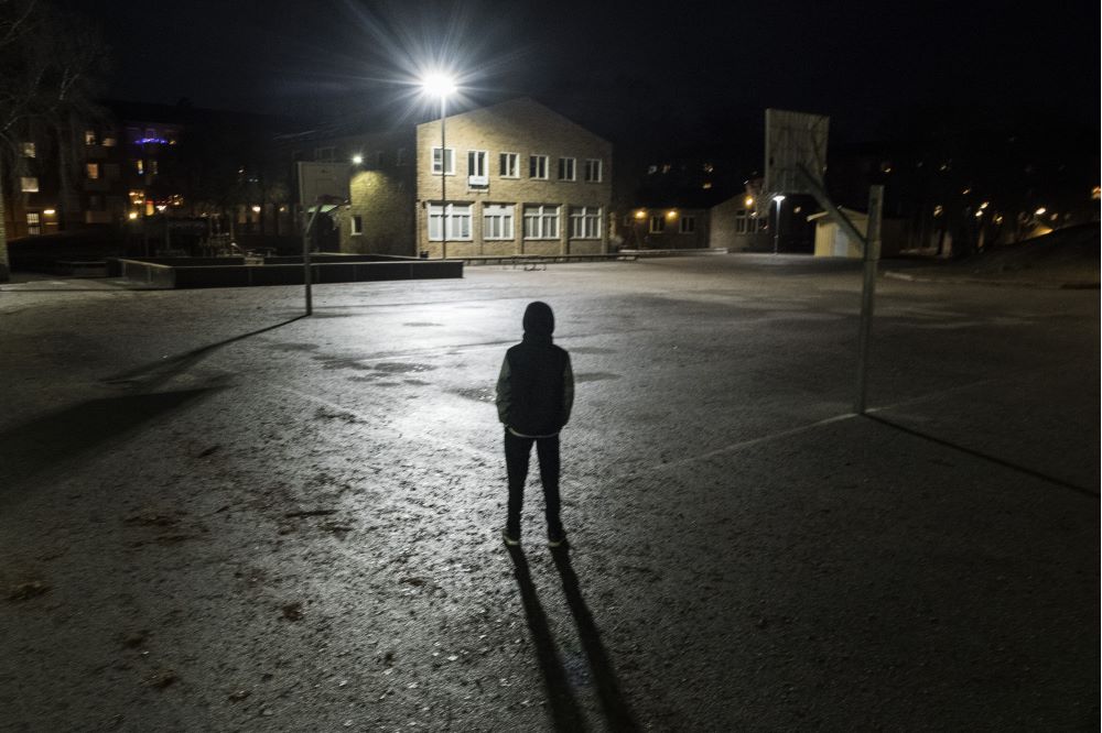 En ensam ung pojke står i mörkret på en skolgård. Arrangerat foto.