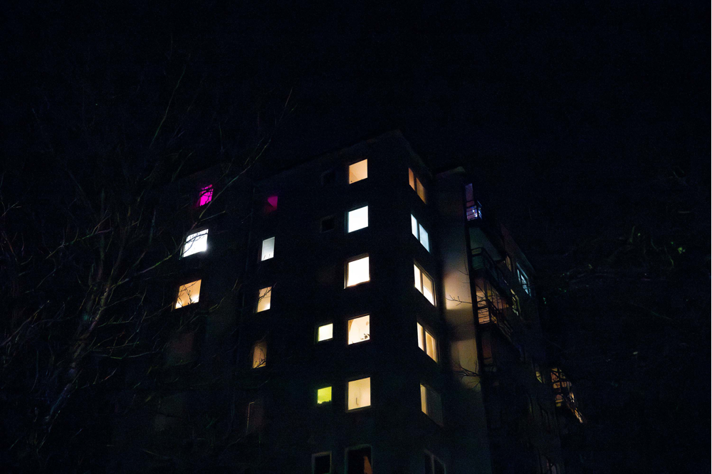 Ett flerfamiljshus med upplysta fönster ses nedifrån gatan. Foto.