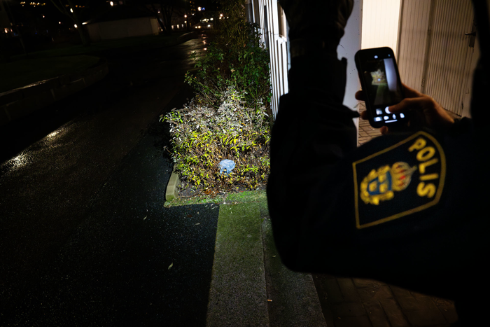 Man ser den uniformsbeklädda armen på Kenny Adersjö när han med tjänstemobilen dokumenterar ett fynd i form av en plastpåse i buskarna framför honom. Foto.
