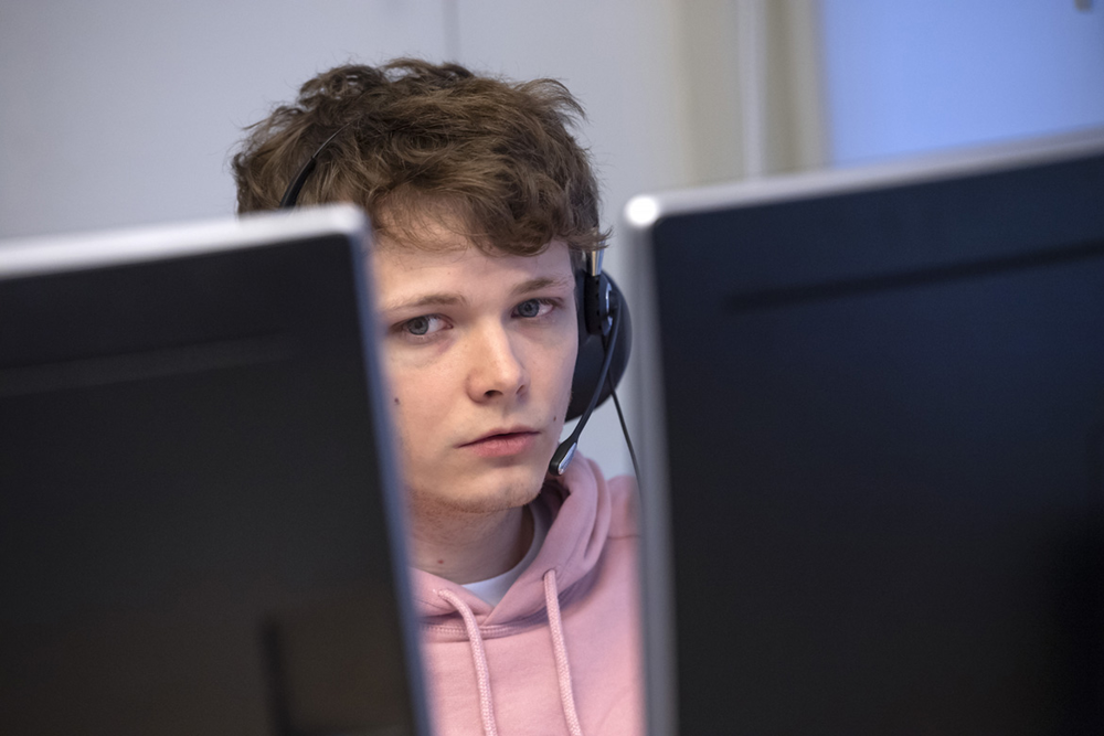 Mellan baksidorna på två bildskärmar ser man Kalle Haag Nilsson med headset på huvudet