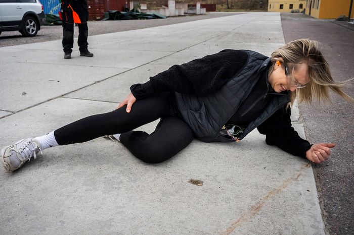 Figuranten/kommunikatören Rönna Wernbom ligger på betongplattor med skjutet ben i ett övningsscenario. Foto.