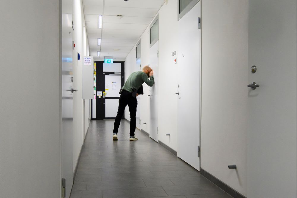 Utredaren Fredrik Ståhl ses kika in genom en tittlucka i en dörr. Foto.