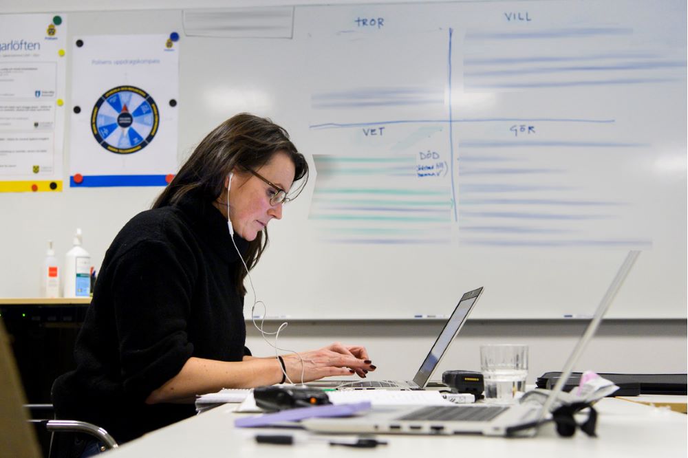 Biträdande kriminalinsatschef Linda Borgsved sitter vid datorn framför en whiteboardtavla med orden tror, vet, vill och gör. Foto.
