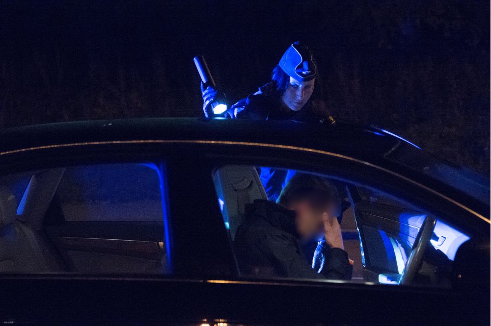 En bil har stoppats en mörk kväll av en polispatrull och poliskvinnan lyser in mot föraren med sin ficklampa. Foto.