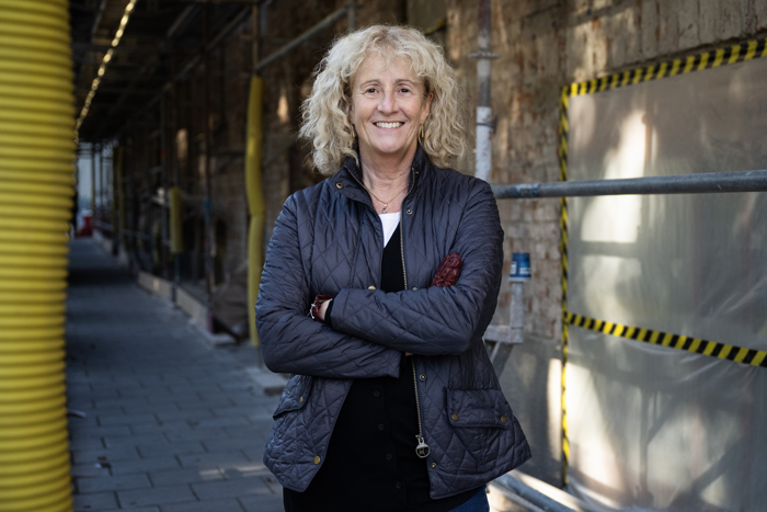 Cecilia Forzelius står utanför en tegelbyggnad med en byggnadsställning. Foto.