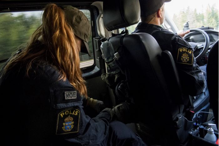 Polisen Jenny sitter i baksätet i en polisbil med en manlig kollega framför på förarsätet. Foto.