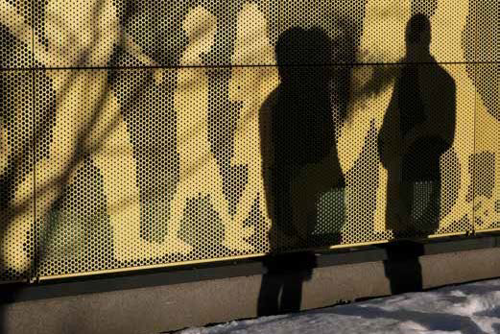 Två svarta siluetter av människor ses framför ett myller av gula siluetter av människor. Illustration.