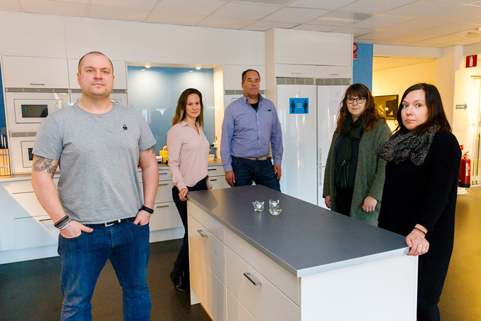 De fem utredarna i arbetsgruppen står i köket på sin arbetsplats. Foto.