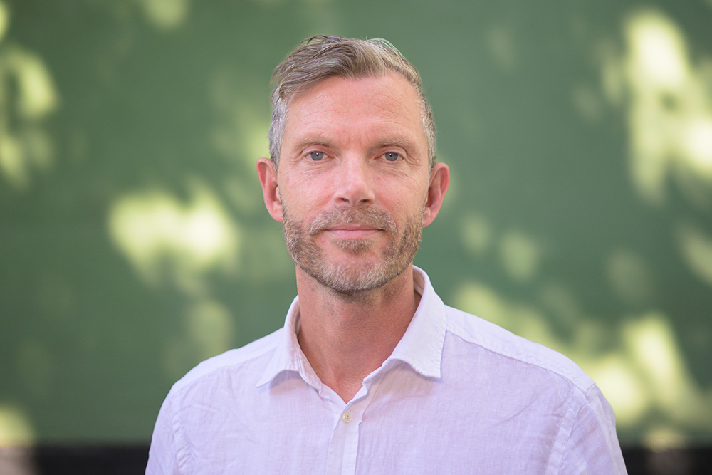 Patrik Larsson utomhus med grönskande bakgrund. Foto.