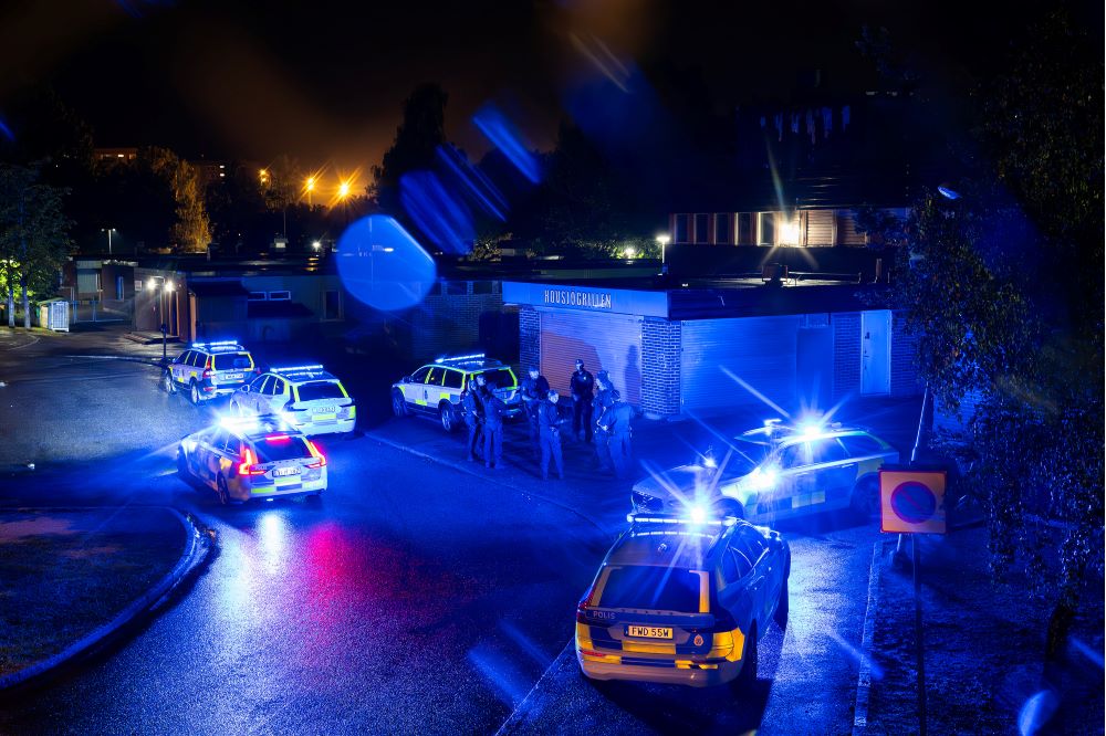 Flera polisbilar och poliser samlade på en gata utanför ett stängt gatukök på kvällen. Foto.