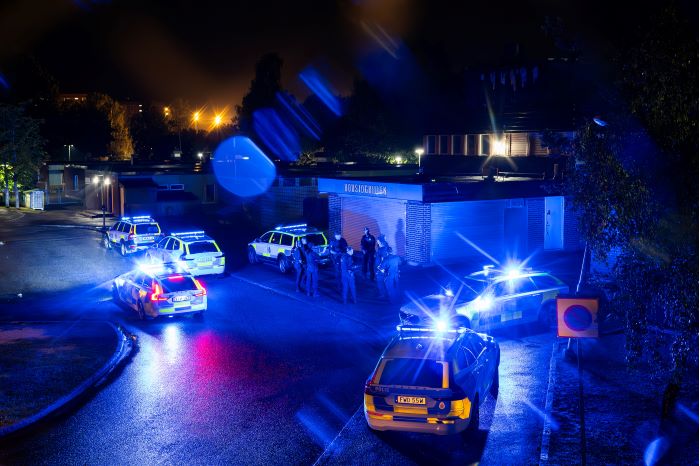 Flera polisbilar och poliser samlade på en gata utanför ett stängt gatukök på kvällen. Foto.