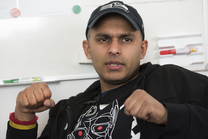 Polisen Simon Häggström sitter i ett mötesrum, med en whiteboardtavla i bakgrunden. Han har en mörk luvtröja och keps på huvudet.