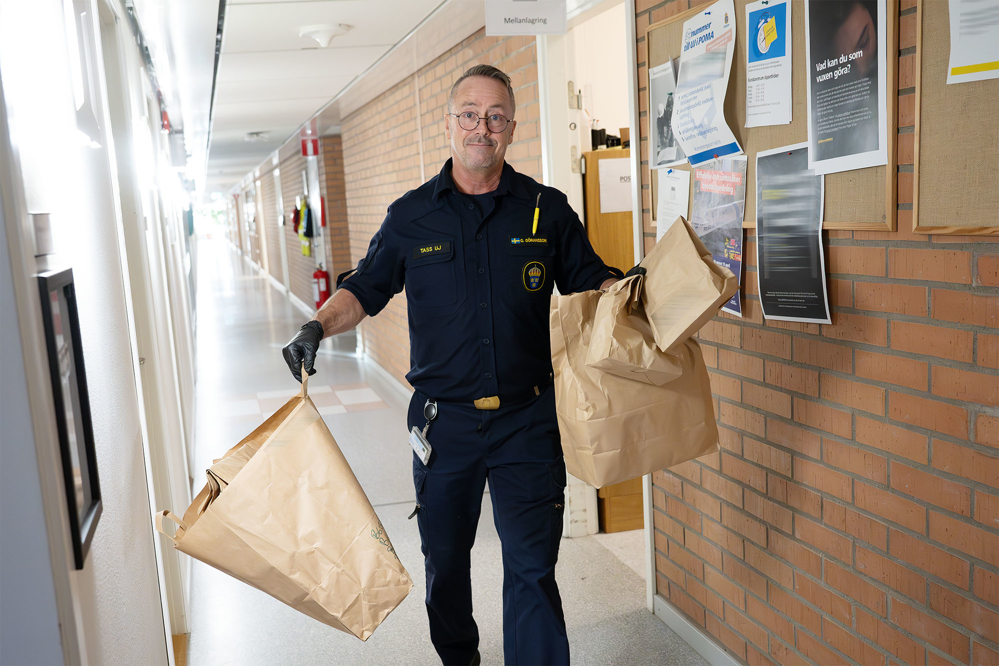 Glenn går i korridoren från beslagsrummet med ett gäng papperskassar i händerna. Foto.