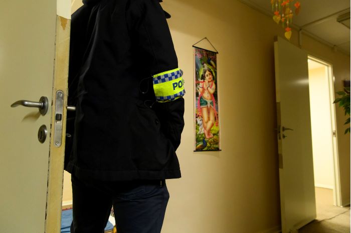 En civilklädd polis med armbindel där det står "polis"  står i korridoren och bevakar de öppna rummen. Foto.