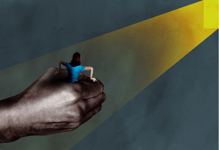 En kvinna hålls fast upp till midjan i en jättelik knuten manshand och försöker ta sig ur greppet. Illustration.