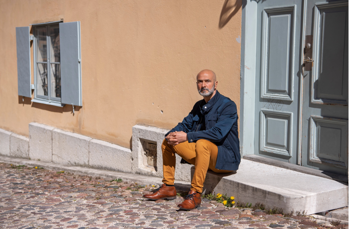Ayman Aboulaich sitter på en trappa utanför ett hus med putsad fasad. Foto.