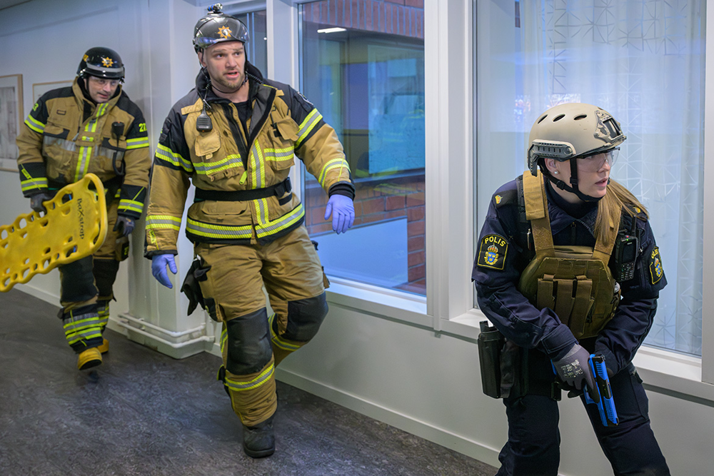 En polis går först och kollar att korridoren är säker och två från räddningstjänsten går bakom med en tom bår. Foto.
