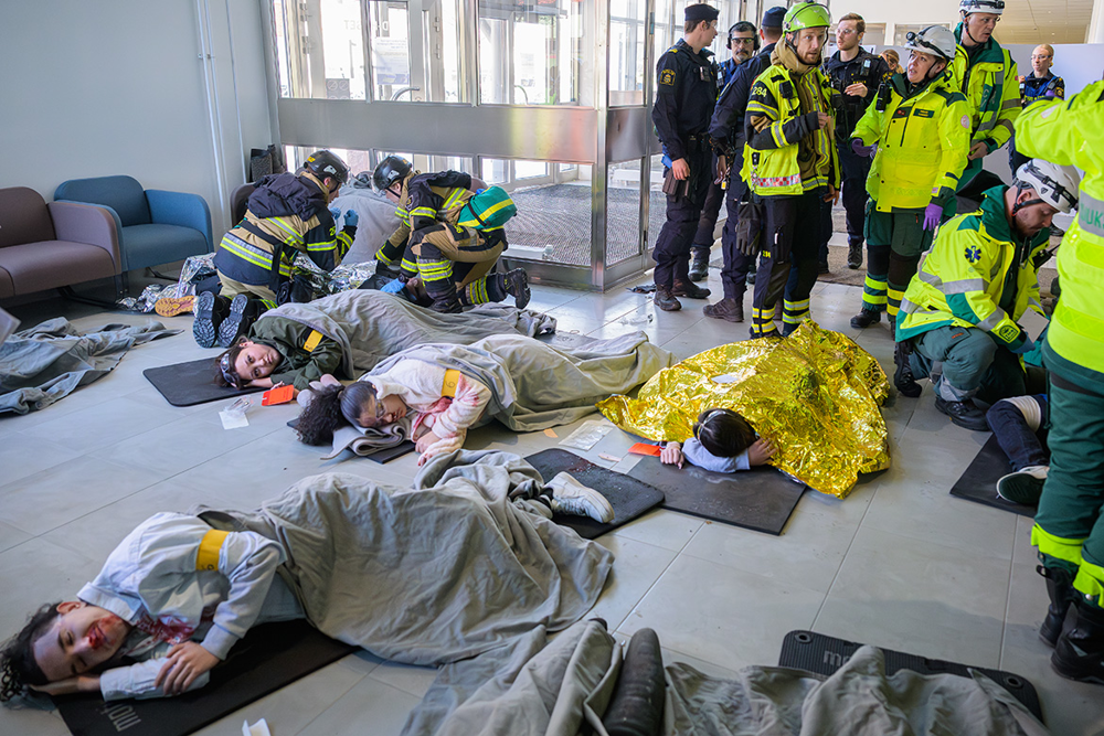 Figuranter som spelar skadade ligger utplacerade på liggunderlag på golvet och räddningstjänst och ambulans arbetar med skadade. Foto.