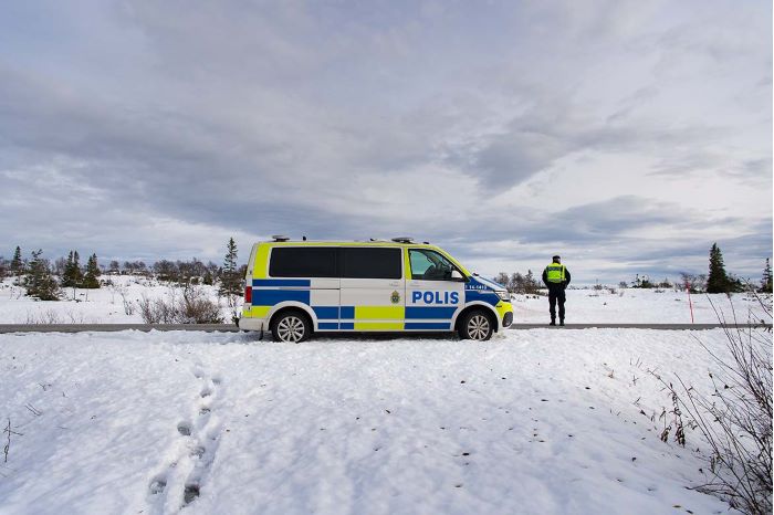 En polis står vid en polisbuss i ett snöigt landskap. Foto.