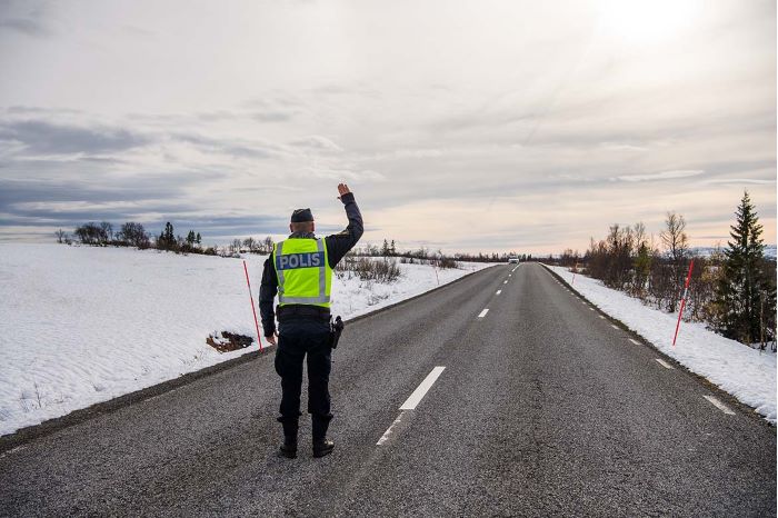 En polis håller upp sin högra hand mot en bilist för att stoppa den för en gränskontroll. Foto.