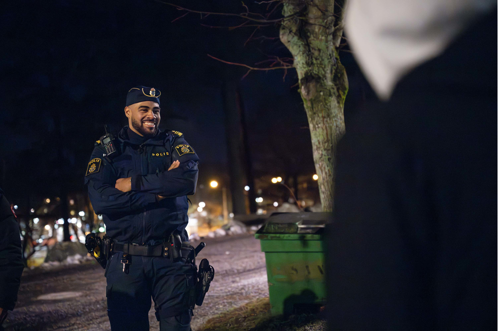 Patrick Tornéus står utomhus i mörkret vid en grusväg och och pratar med en tonåring som vi ser ryggen på. Foto.