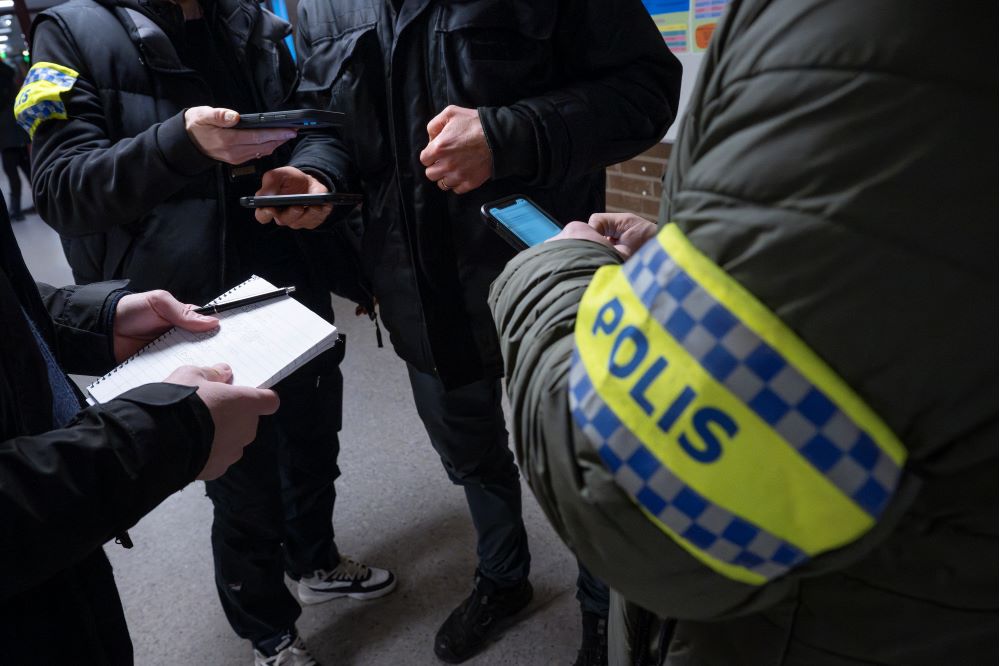 Händer och armar syns på fyra poliser som står i ring. Foto.