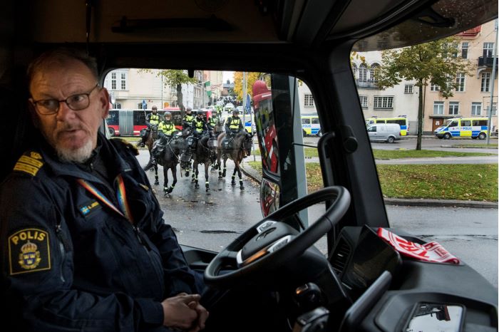Kommissarie Anders "Jasse" Jansson på förarplatsen i den parkerade lastbilen, där sex polisryttare på sina polishästar syns genom fönsterrutan. Foto.