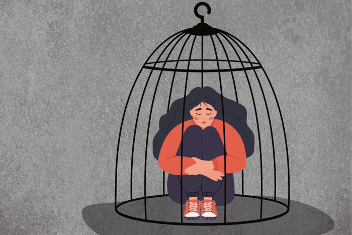 En flicka sitter med händerna runt benen och nedslagna ögon i en stängd fågelbur. Illustration.