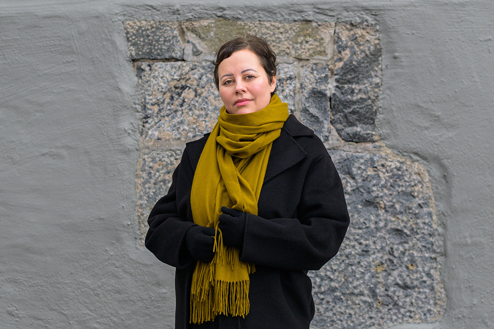 Sofia Zitouni står utomhus framför en stenvägg. Foto.