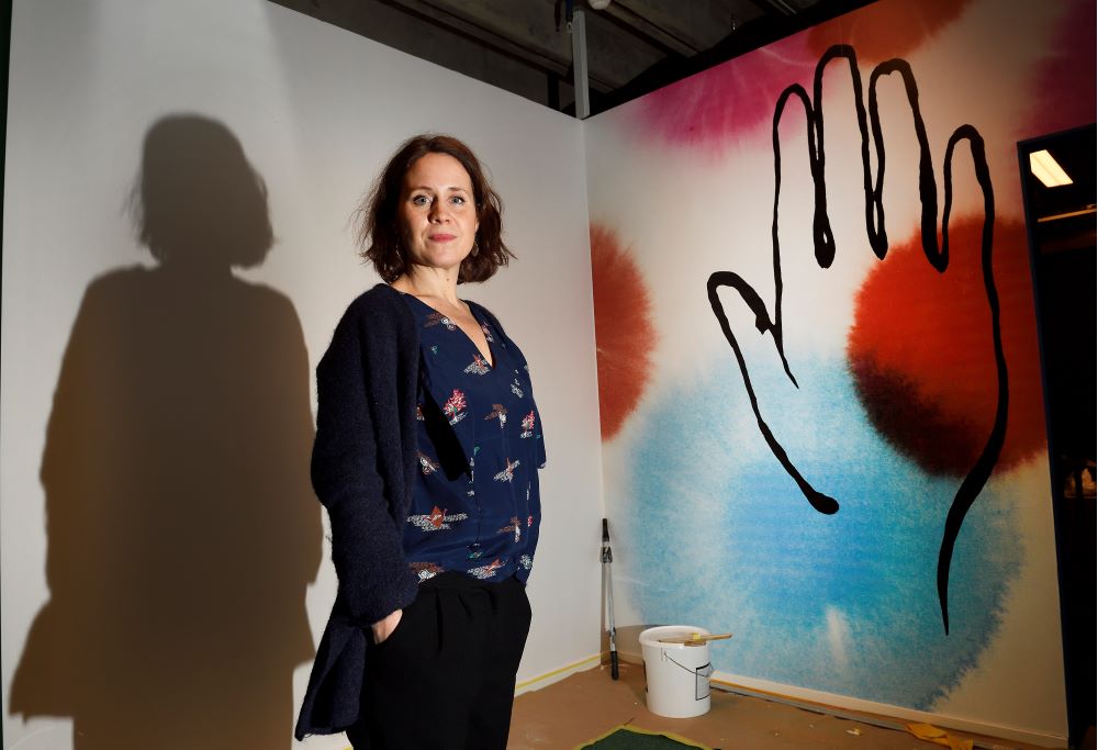 Tina Landgren står framför en vägg. Väggen är målad med en hand i siluett.