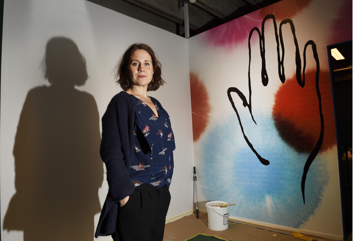 Tina Landgren står framför en vägg. Väggen är målad med en hand i siluett.