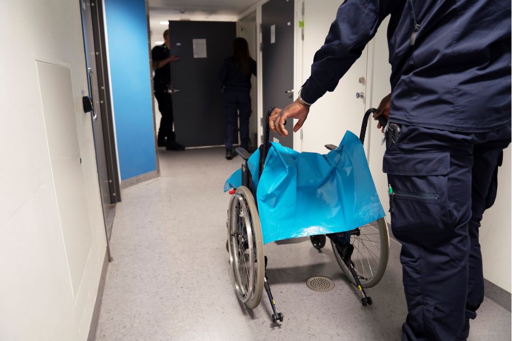 Arrestvakten Abdoulie Sarr  för en rullstol i en korridor. Foto.