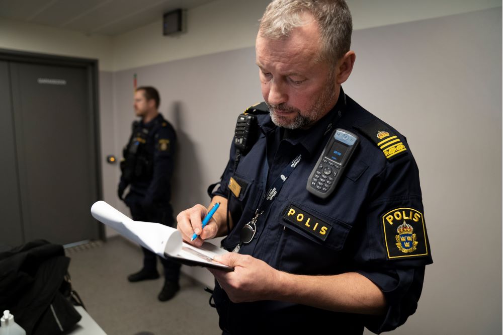 Stationsbefäl Thomas Brandt står och antecknar något med papper och penna. Foto.