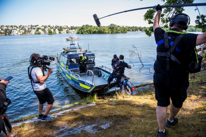 Sjöpoliserna bär upp en moped på polisbåten medan produktionsbolaget filmar och tar upp ljud. Foto.