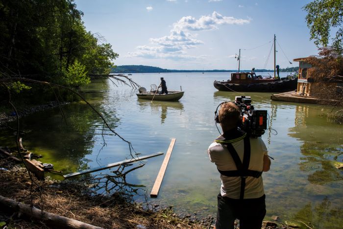 En fotograf filmar ut över vattnet när sjöpolisen Samuel Sjöö stakar ut en båt. Foto.