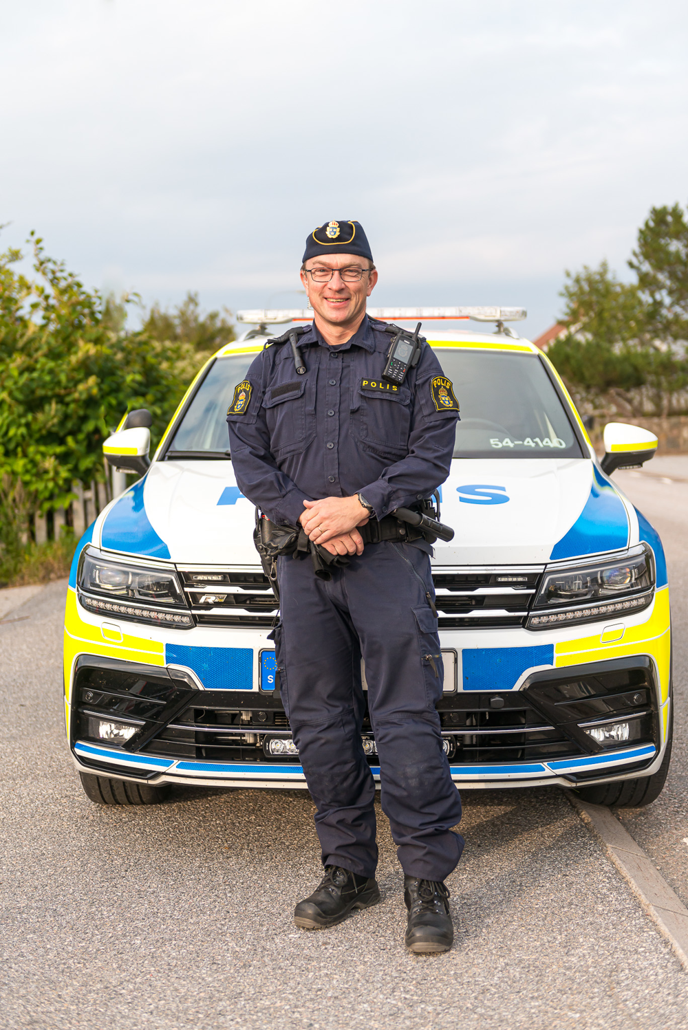 Polisen Andreas framför en polisbil.
