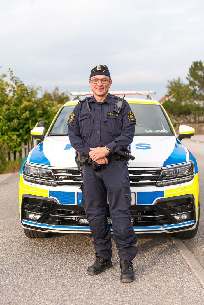 Polisen Andreas framför en polisbil.