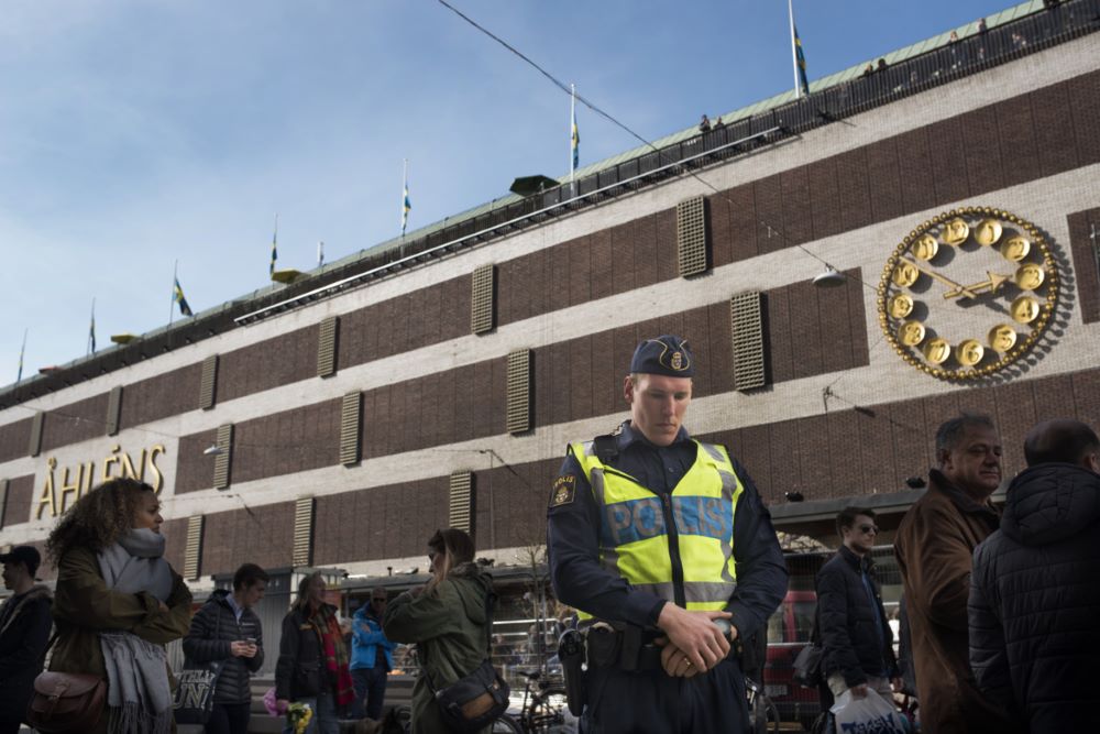 Andreas Snöberg står med händerna knäppta och böjt huvud utanför Åhlens city i Stockholm, under den tysta minuten som hölls för att hedra offren på Drottninggatan. Mellan Andreas och varuhuset rör sig flera människor.
