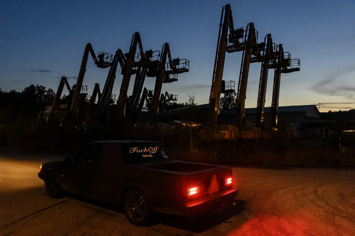 En a-traktor kör förbi ett industriområde i skymningen. Foto.