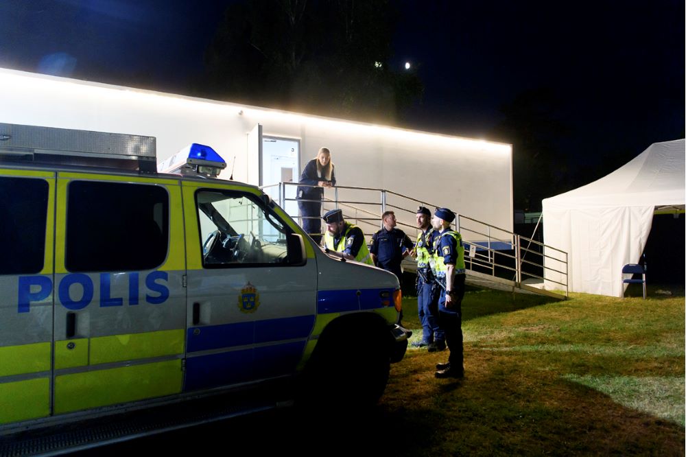 Utanför trailern står en polisbuss och tre IGV-poliser på gräsmattan. Cecilia Carlsson och Peter Storm väntar vid räcket till trailern. Foto.