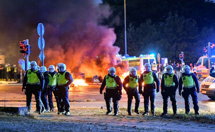 En grupp poliser skyddade med hjälm framför eld och rök. Foto.