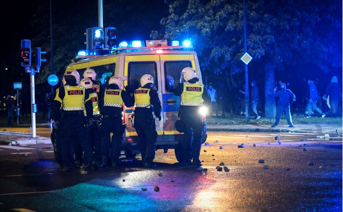 En grupp poliser tar skydd bakom en polisbuss. Foto.